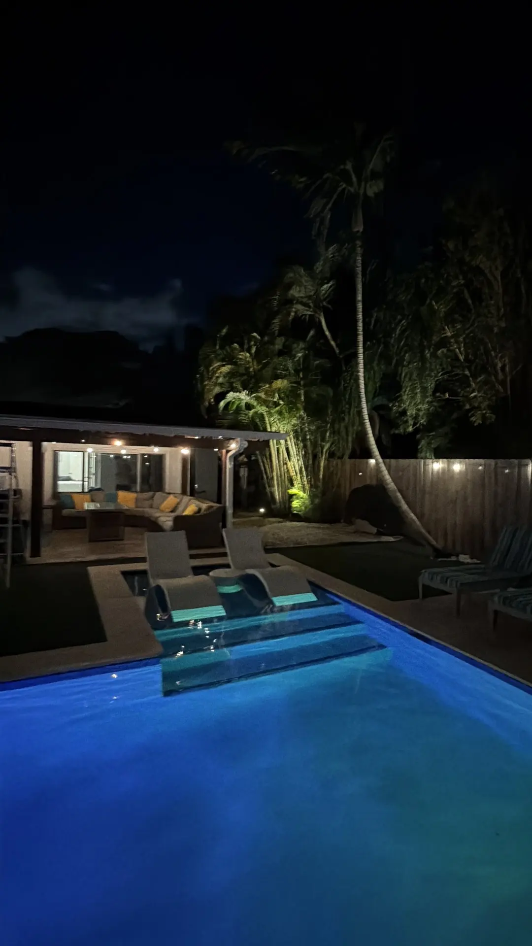 The pool steps and sun shelf glowing blue at night, the covered patio beyond