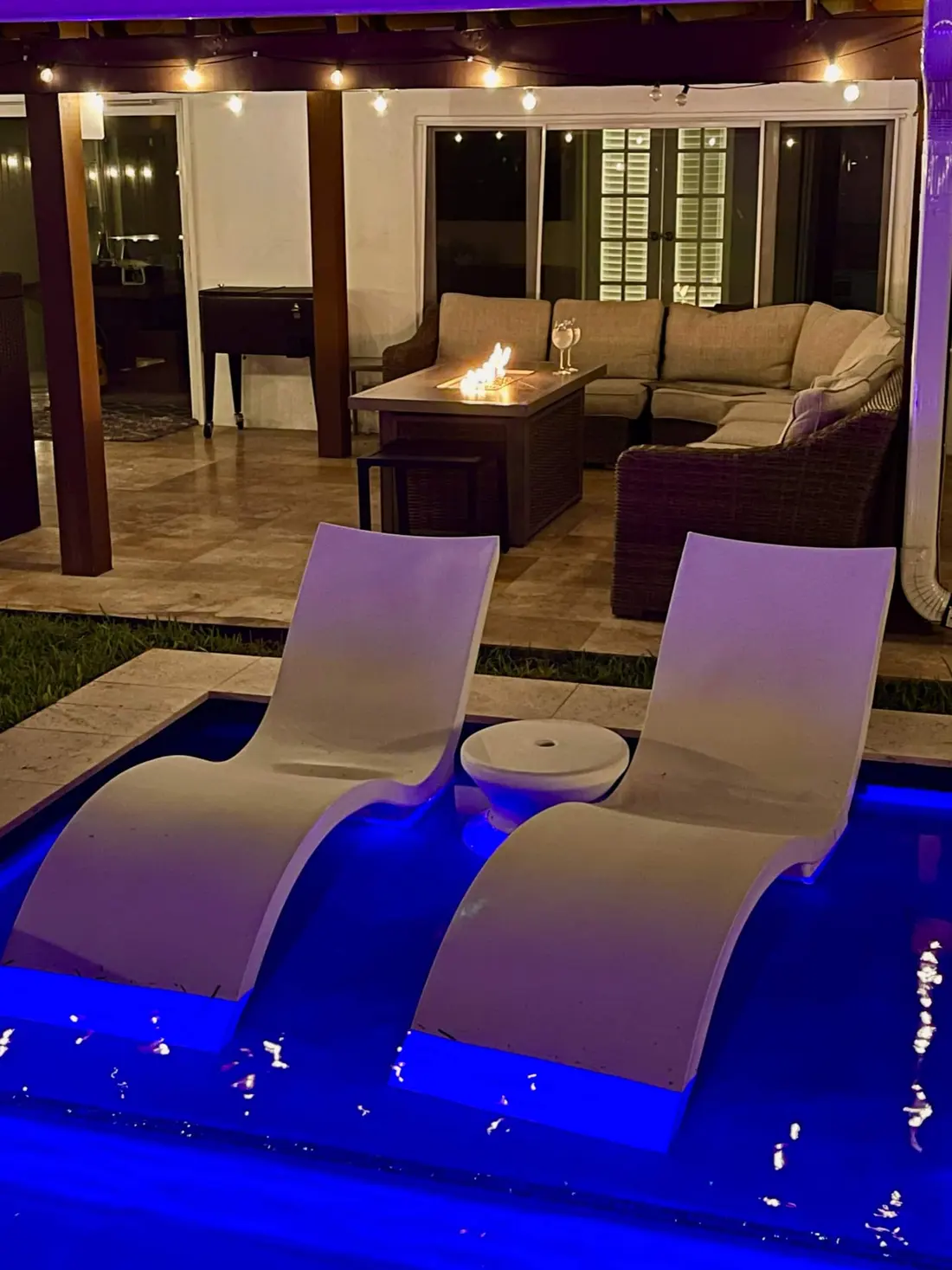 The pool and loungers lit deep blue at night under the covered patio