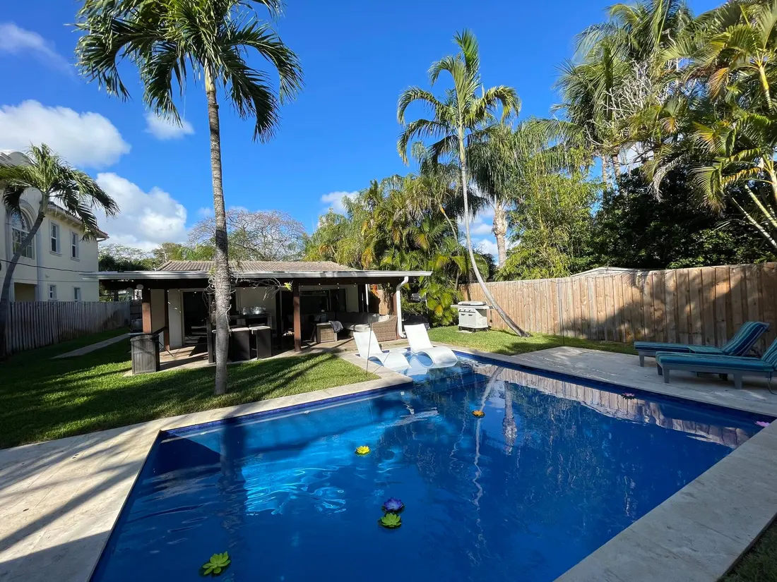 Sunlit pool with lounge chairs and palm trees in the private backyard