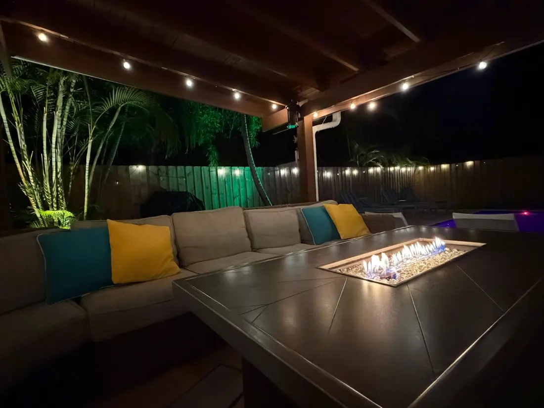The fire table lit under the covered patio, the sectional and green-lit bamboo behind it