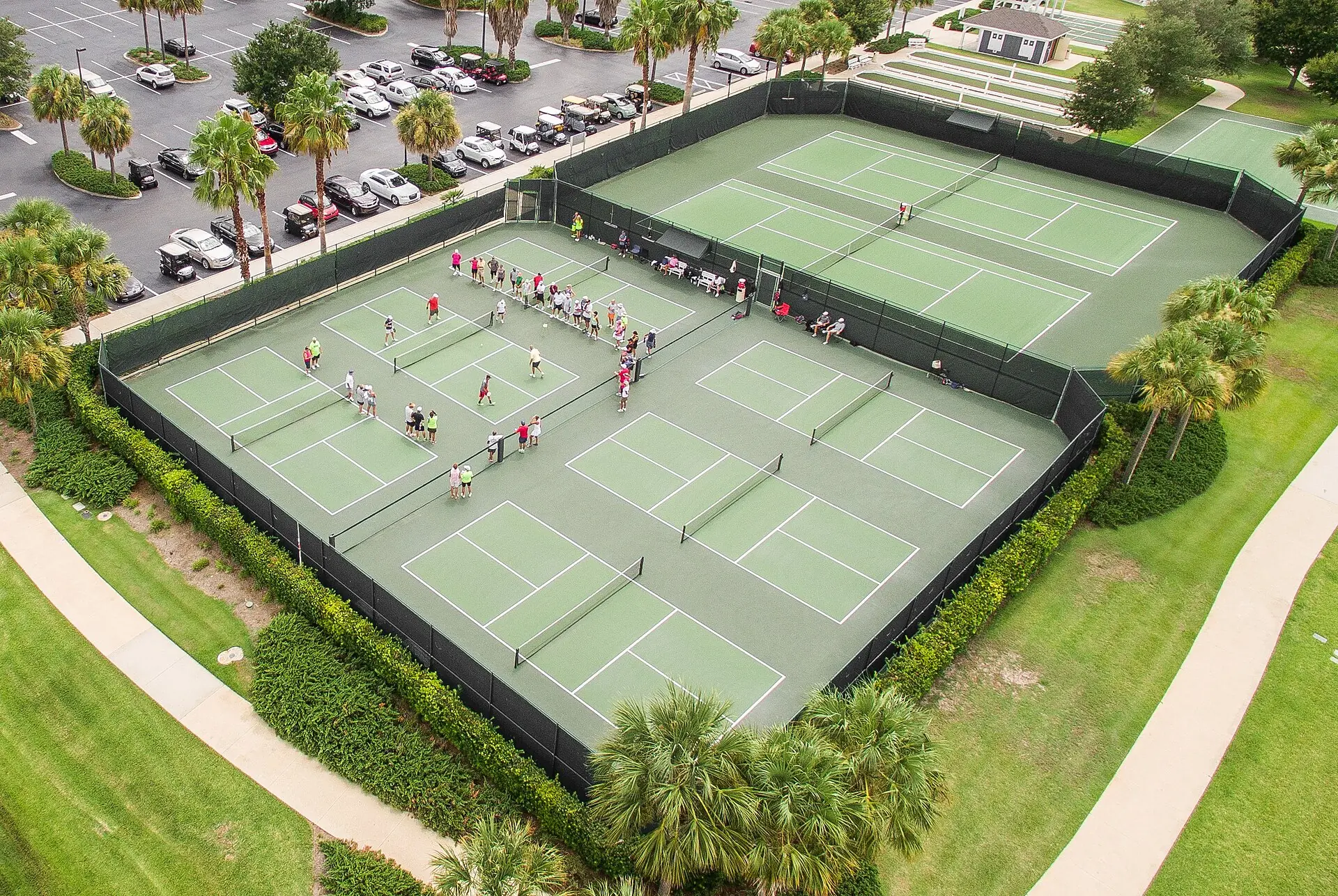 Jimmy Evert Tennis Center: aerial drone view of outdoor pickleball and tennis courts surrounded by palms, parking lots, and walkways