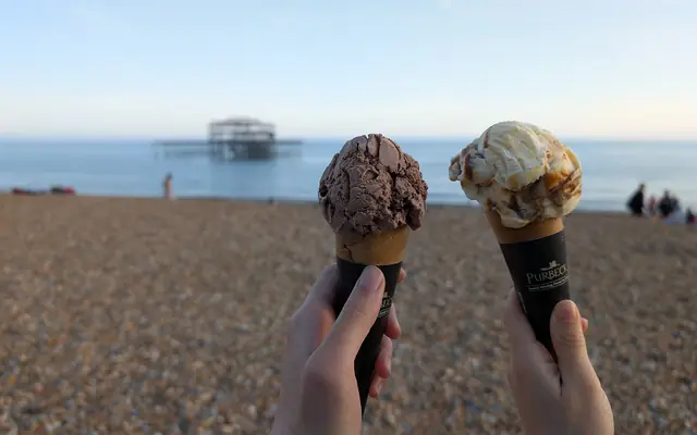 Two ice cream cones held up against a beach and the sea
