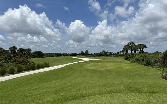 Plantation Preserve Golf Course & Club: a wide view across a manicured golf course fairway and cart path lined with native vegetation and palm trees under a sky filled with cumulus