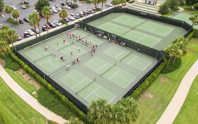 Jimmy Evert Tennis Center: aerial drone view of outdoor pickleball and tennis courts surrounded by palms, parking lots, and walkways