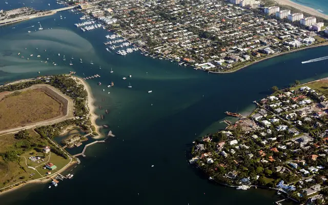 An aerial view of Jupiter Inlet and the surrounding residential communities and waterways in Palm Beach County, Florida, including the historic red Jupiter Inlet Lighthouse on the 