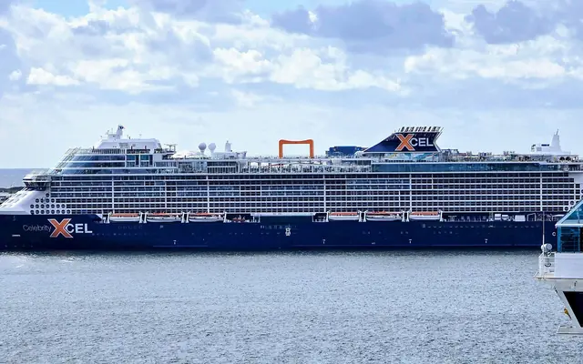 A large Celebrity Cruises Edge-class ship docked in the waterway at Port Everglades under cloudy skies