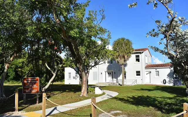 The Terramar Visitor Center and administration building at Hugh Taylor Birch State Park surrounded by subtropical trees and lawn under a clear blue sky