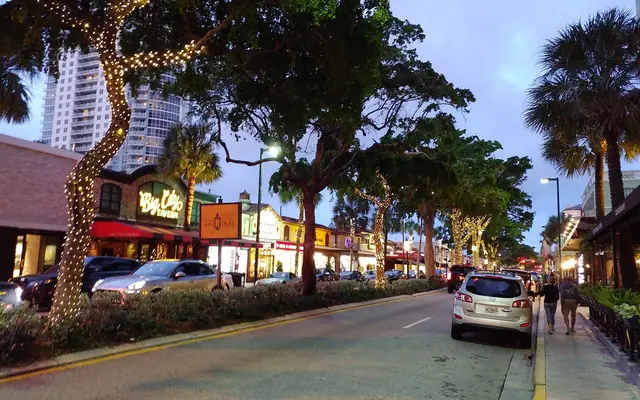 A tree-lined street at twilight featuring shops and restaurants including Big City Tavern on Las Olas Boulevard