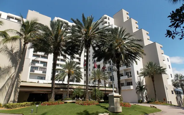 Port Everglades: a large multi-story beach resort hotel entrance with palm trees, manicured lawns, and a circular driveway under a clear blue sky