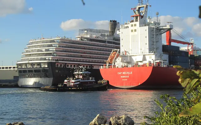 Port Everglades: a large cargo ship, a tugboat, and a Holland America Line cruise ship docked in a busy port basin viewed across the water