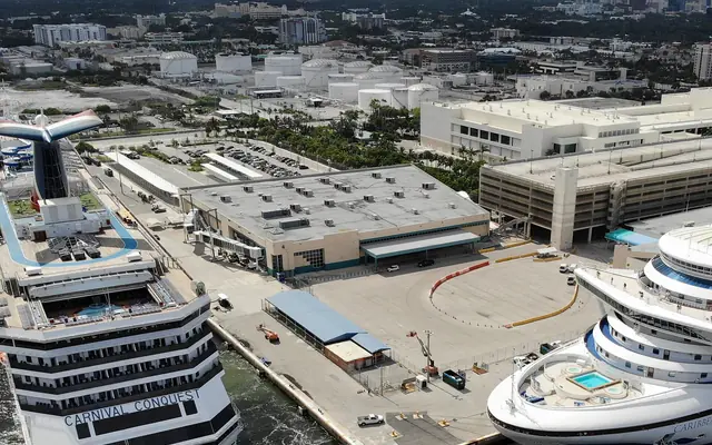 Aerial view of cruise ships docked at Port Everglades terminal berths with industrial storage tanks and urban flatlands in the background