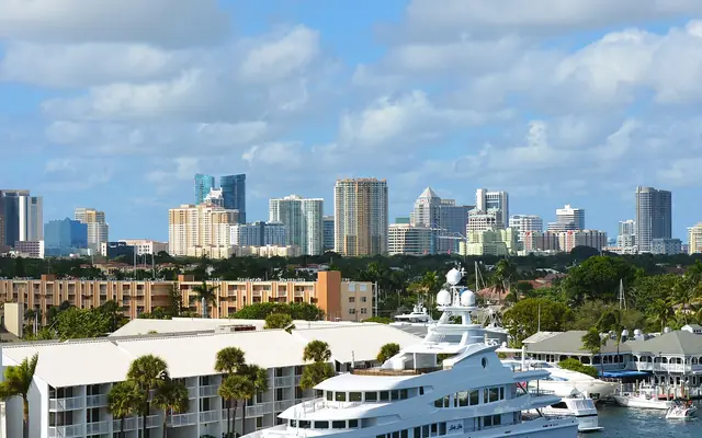 A daytime view across a marina with a large luxury yacht toward the high-rises of downtown Fort Lauderdale