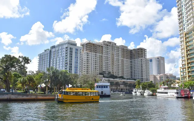 A bright yellow Fort Lauderdale water taxi cruising down the New River with downtown residential high-rises in the background
