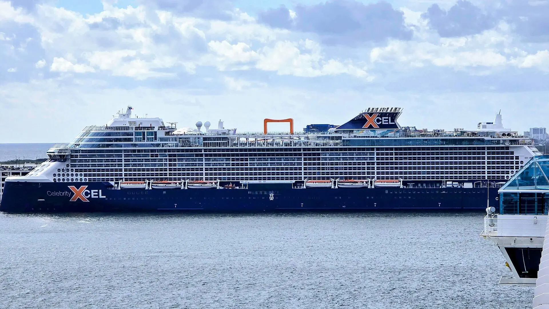A large Celebrity Cruises Edge-class ship docked in the waterway at Port Everglades under cloudy skies