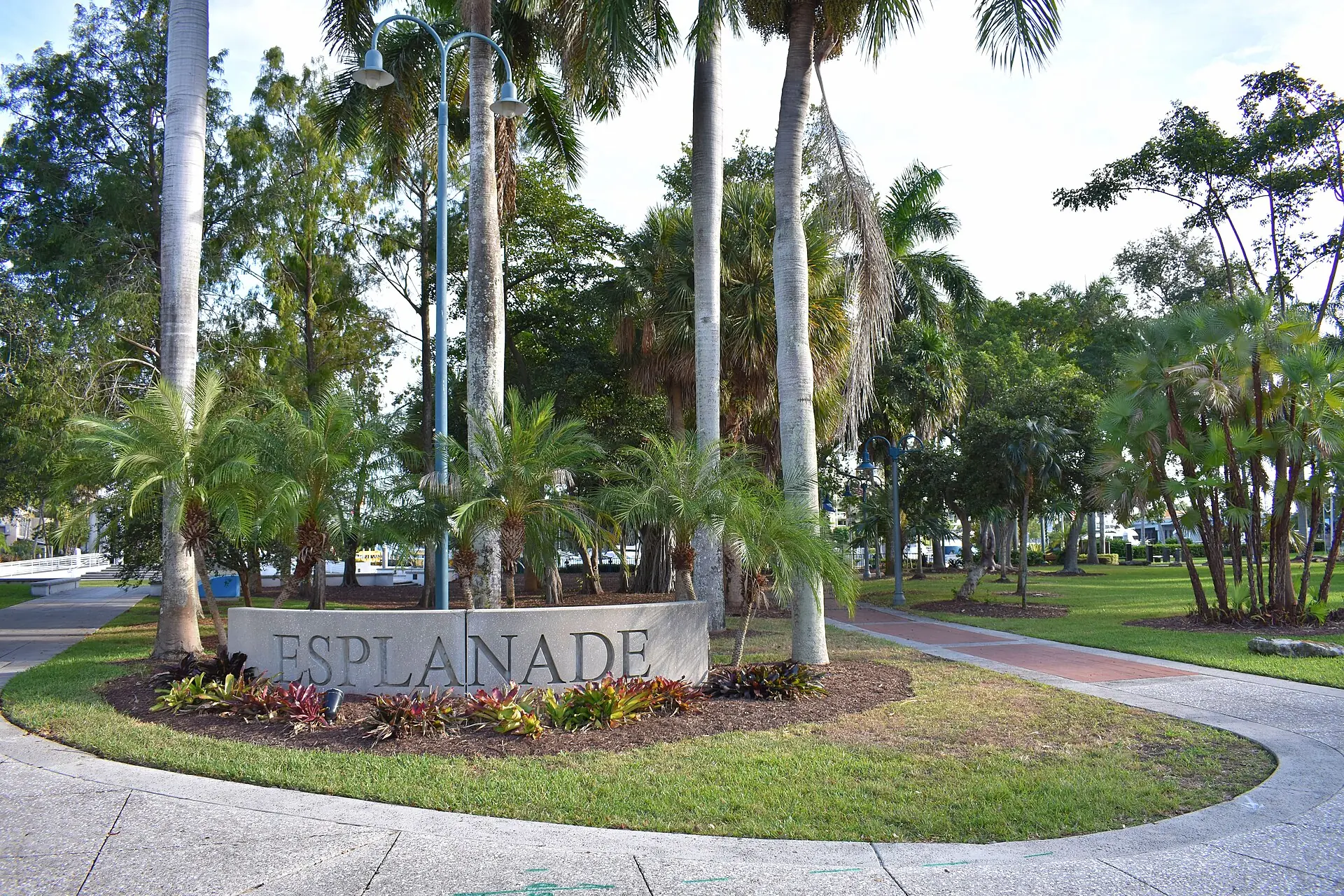 A stone entrance sign reading Esplanade set amid palm trees, manicured lawns, and paved pathways in a park