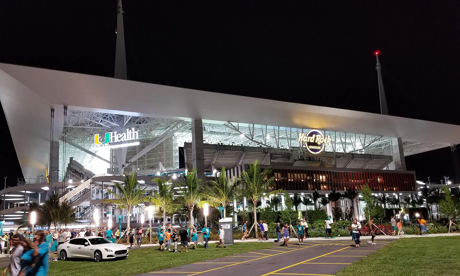 Exterior night view of Hard Rock Stadium illuminated with fans and palm trees outside