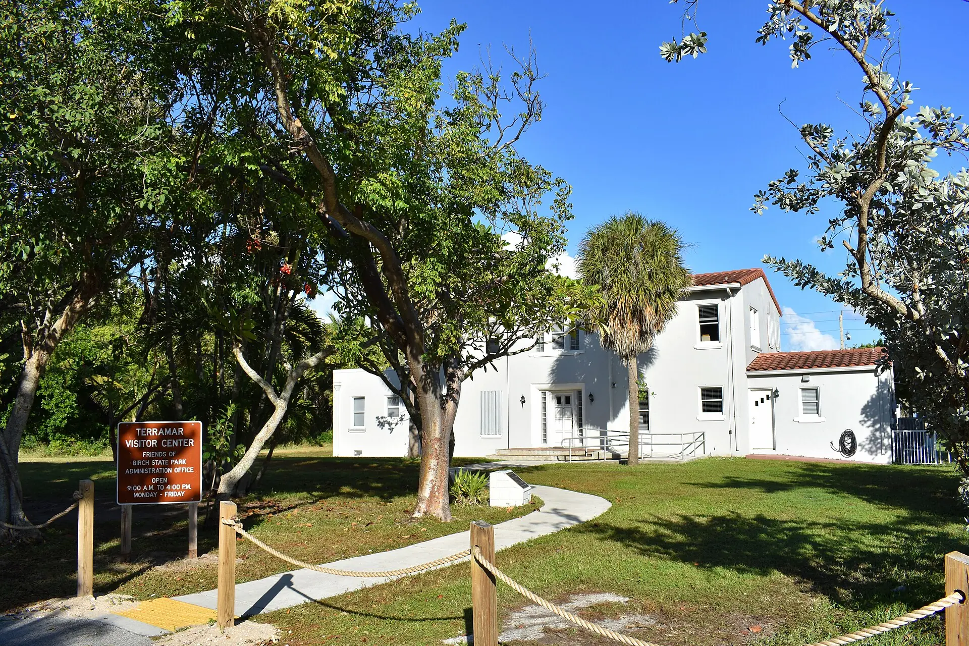 The Terramar Visitor Center and administration building at Hugh Taylor Birch State Park surrounded by subtropical trees and lawn under a clear blue sky