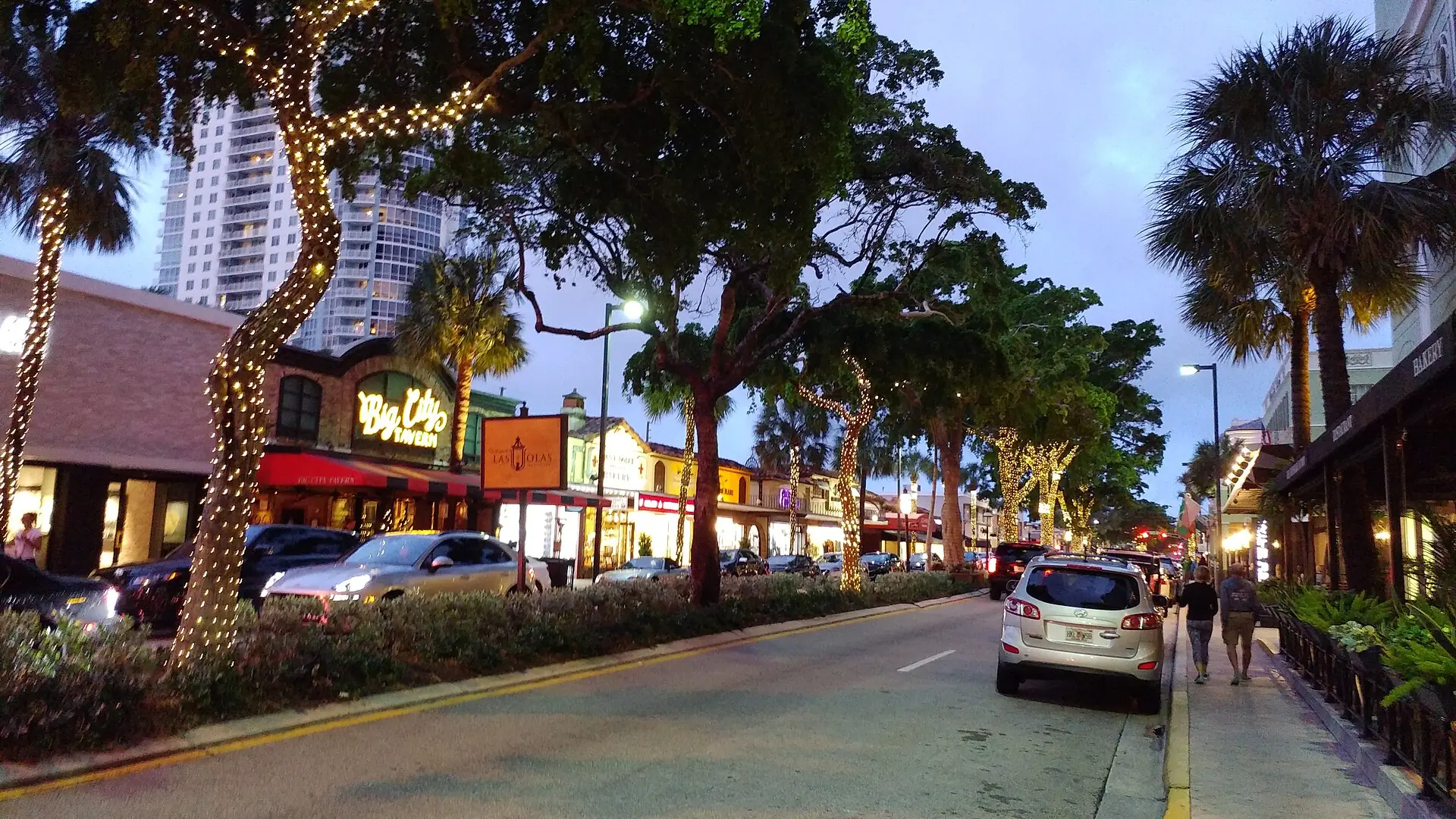 A tree-lined street at twilight featuring shops and restaurants including Big City Tavern on Las Olas Boulevard