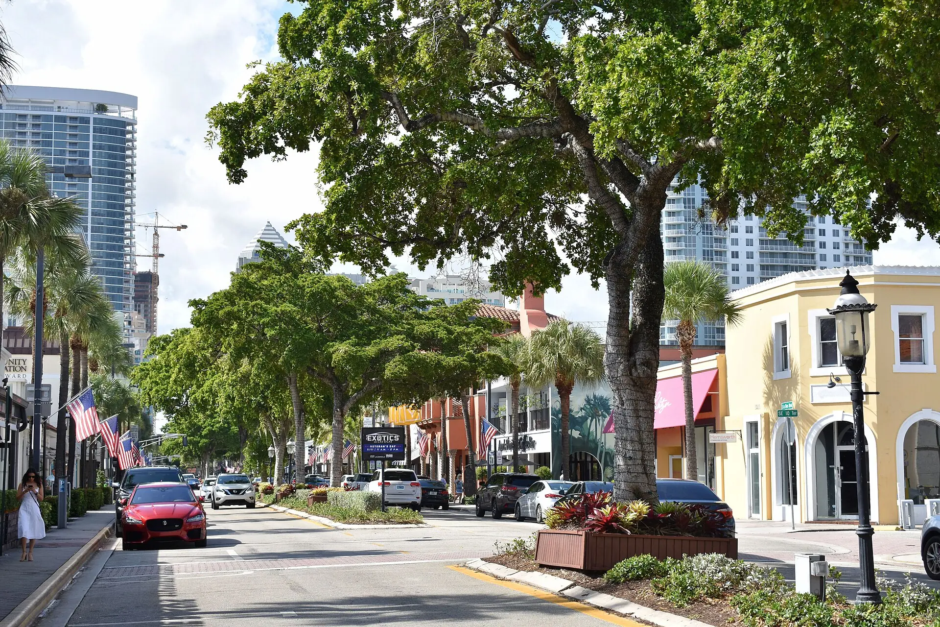A daytime street view down tree-lined Las Olas Boulevard in Fort Lauderdale, showing shops, cars, and downtown towers in the distance