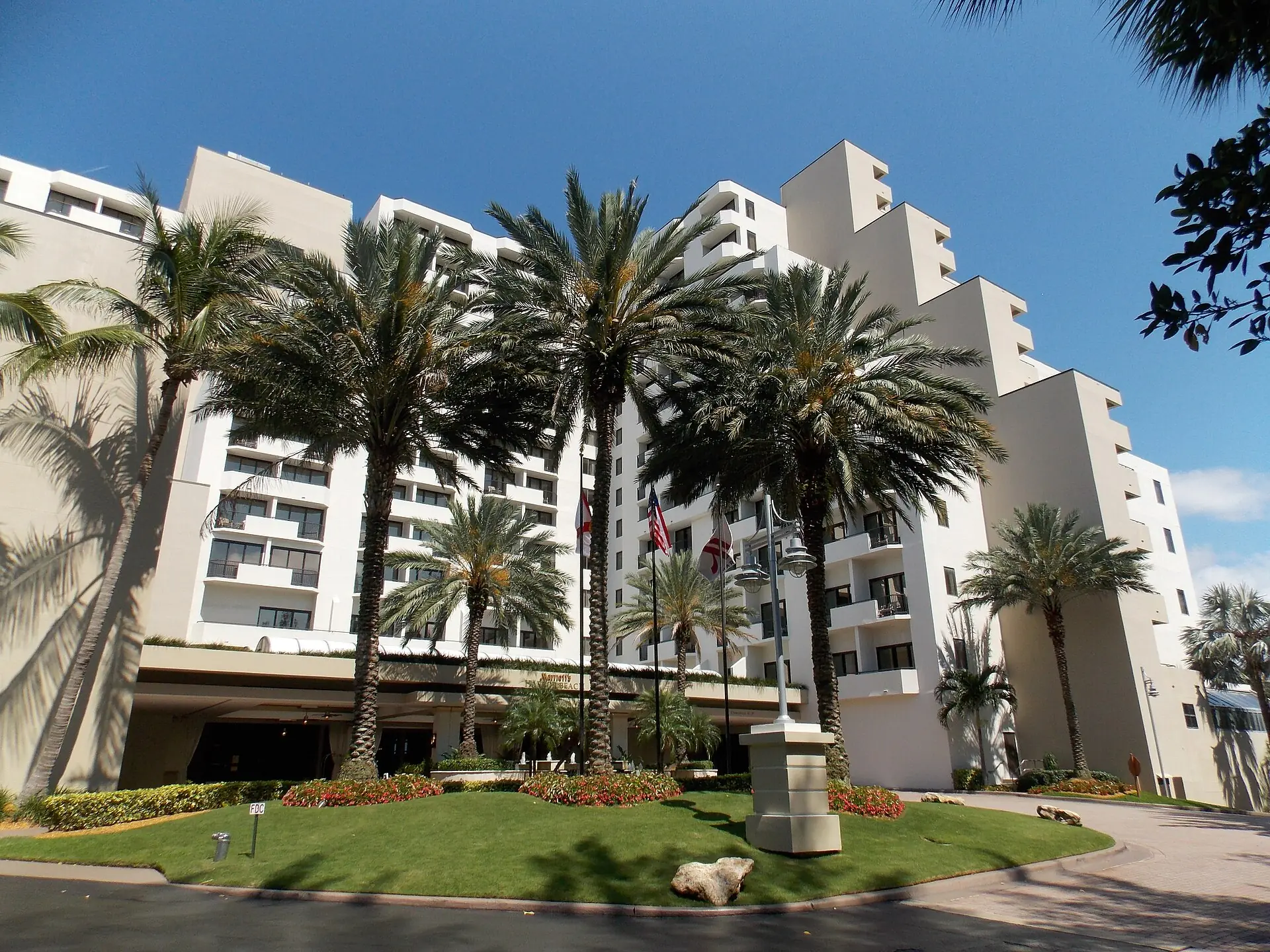 Port Everglades: a large multi-story beach resort hotel entrance with palm trees, manicured lawns, and a circular driveway under a clear blue sky