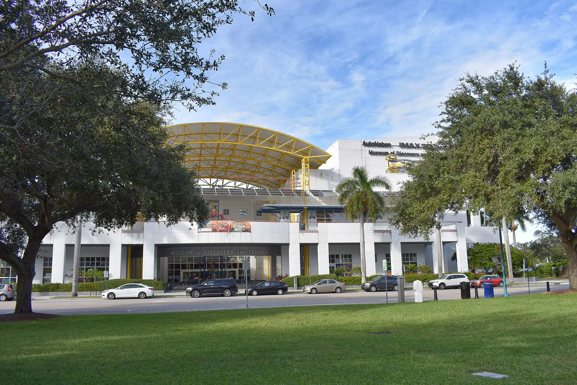 The exterior facade and entrance of the Museum of Discovery and Science in Fort Lauderdale, viewed across a grassy park and street