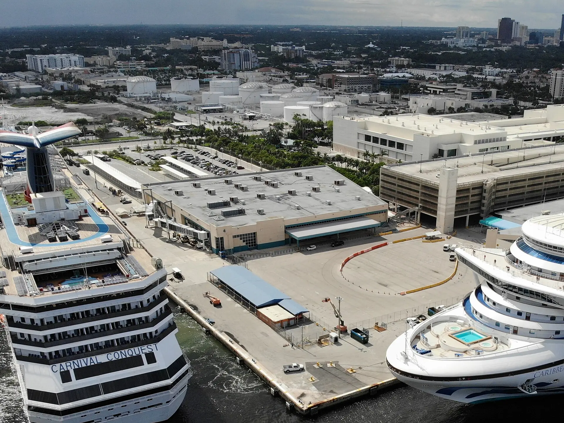 Aerial view of cruise ships docked at Port Everglades terminal berths with industrial storage tanks and urban flatlands in the background