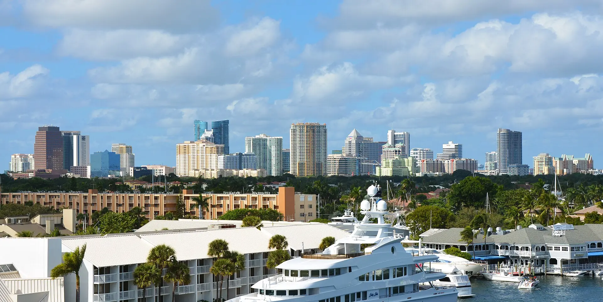 A daytime view across a marina with a large luxury yacht toward the high-rises of downtown Fort Lauderdale