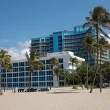 Fort Lauderdale Beach Park: a sandy beach area with palm trees, picnic benches, and beachfront resort hotels under a blue sky