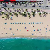 Las Olas Oceanside Park: a top-down aerial photograph of Fort Lauderdale Beach showing State Road A1A, the iconic undulating white wave wall, palm trees, sandy beach with umbrellas