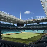 Interior view of Hard Rock Stadium looking across empty seats toward the soccer pitch under a clear blue daytime sky