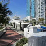 Downtown Riverwalk: a paved promenade along a river marina lined with luxury yachts, palm trees, and modern downtown high-rise condominiums