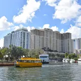 Water Taxi central dock: a bright yellow Fort Lauderdale water taxi cruising down the New River with downtown residential high-rises in the background