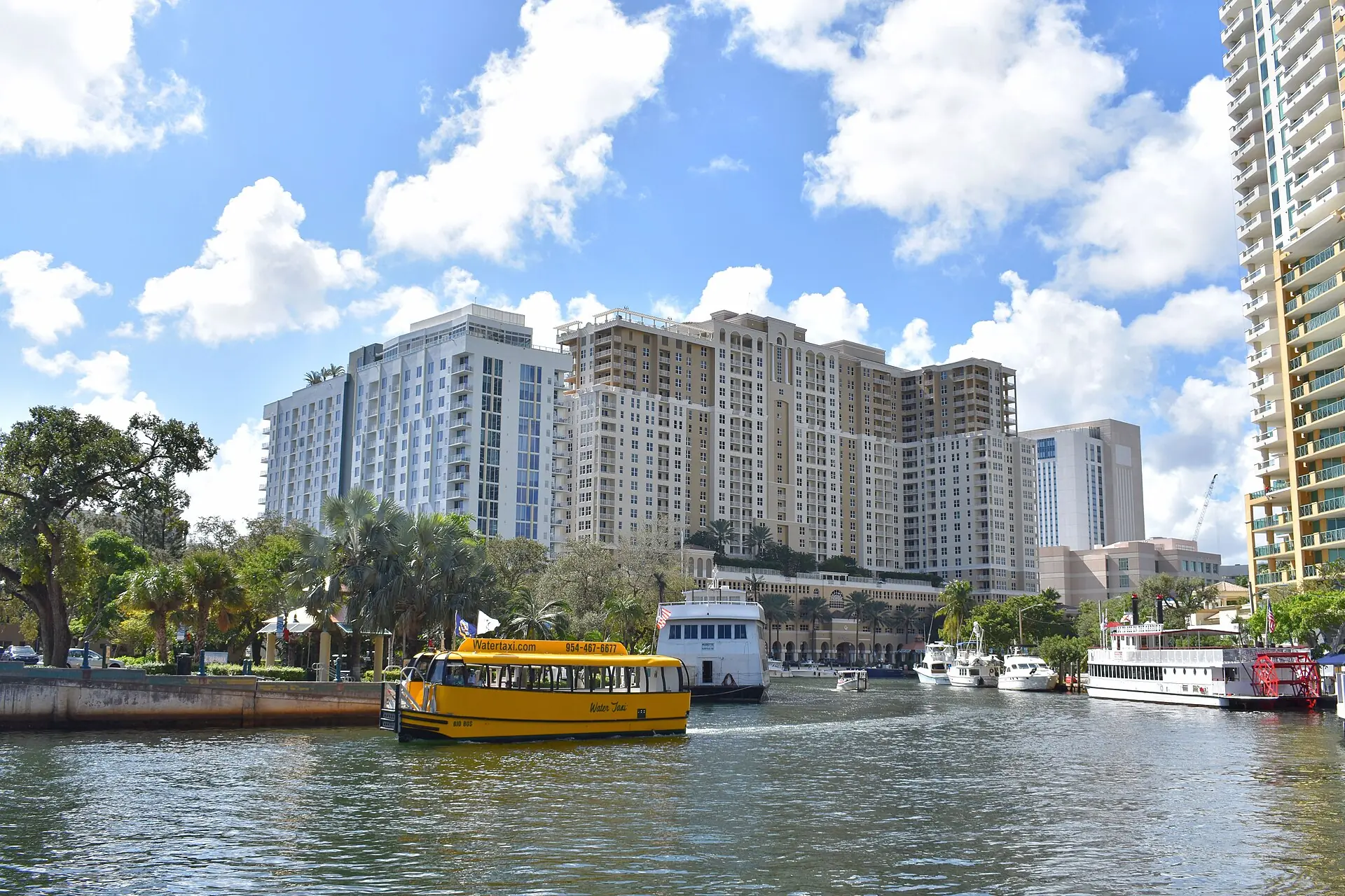 A bright yellow Fort Lauderdale water taxi cruising down the New River with downtown residential high-rises in the background